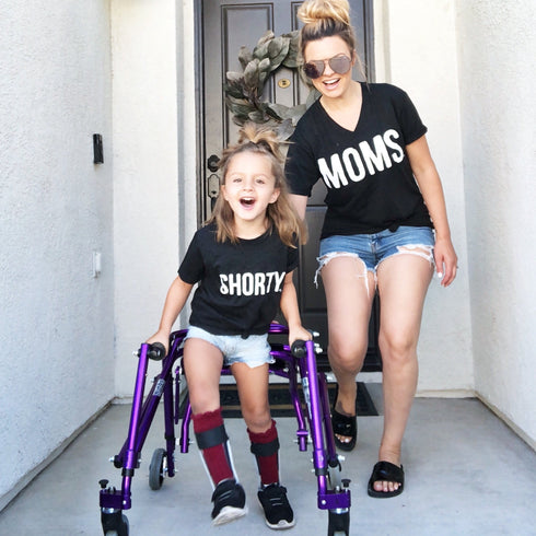 christina smallwood in front of home with daughter that has cerebral palsey wearing matching shirts that say moms and shorty for a cute mommy and me set